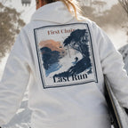 White hoodie with back graphic print; text reads "First Chair" and "Last Run"