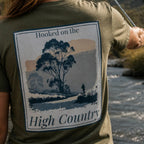 Organic tee in dark olive with “Hooked on the High Country” landscape graphic on front